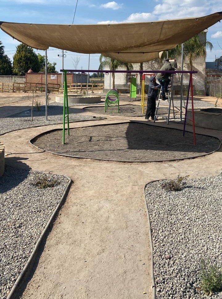 Área de juegos en Parque Cantera, Quintanares, Pedro Escobedo, con estructuras bajo un toldo y caminos de grava